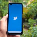 hand holding a smartphone with twitter icon on screen iphone with a social media app logo